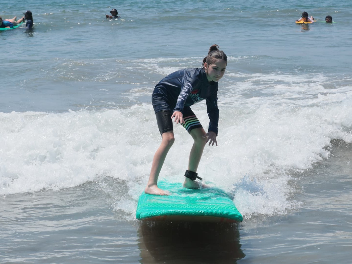 Young girl on a teal surfboard riding a wave during a Dante's Watersports lesson in Manuel Antonio
