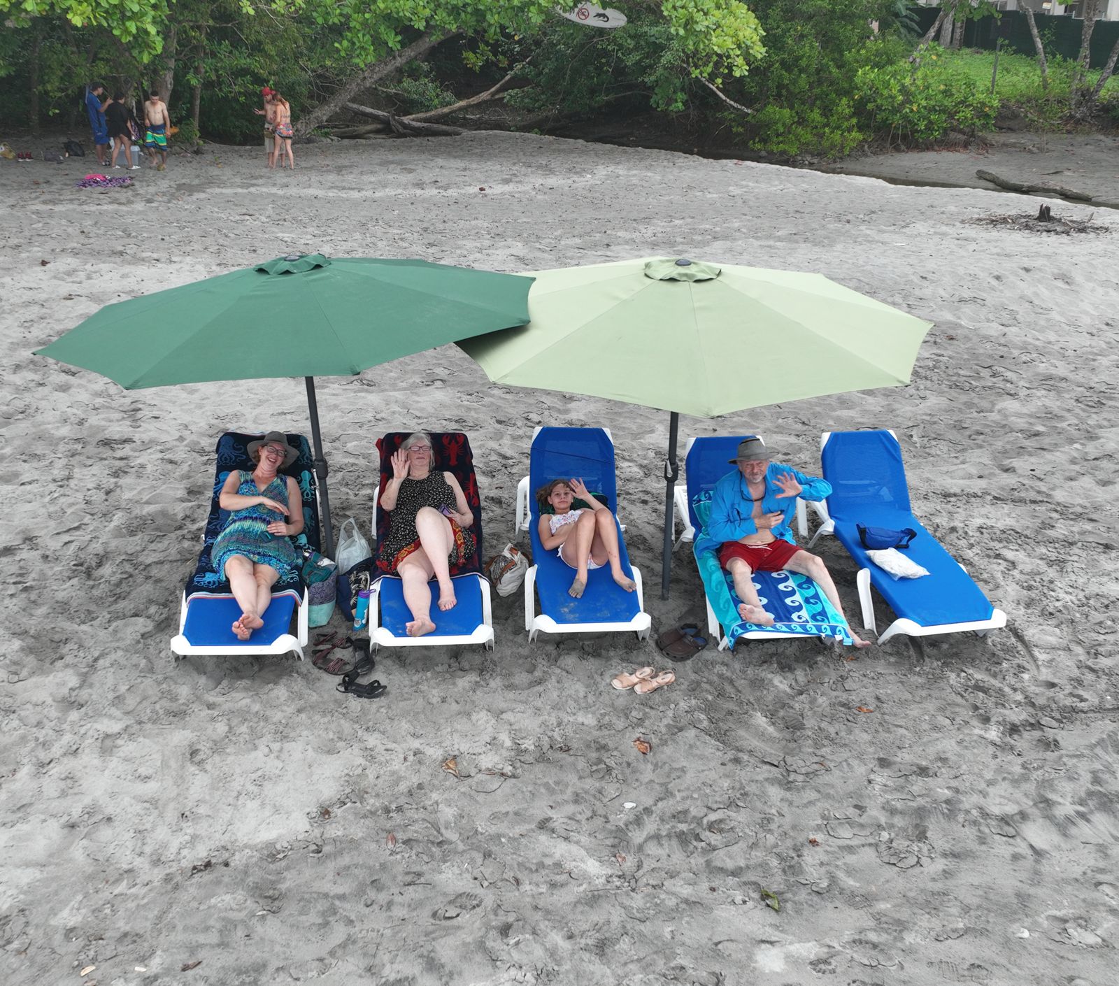 Family relaxing on blue loungers under green umbrellas at Dante's beach setup on Playa Espadilla