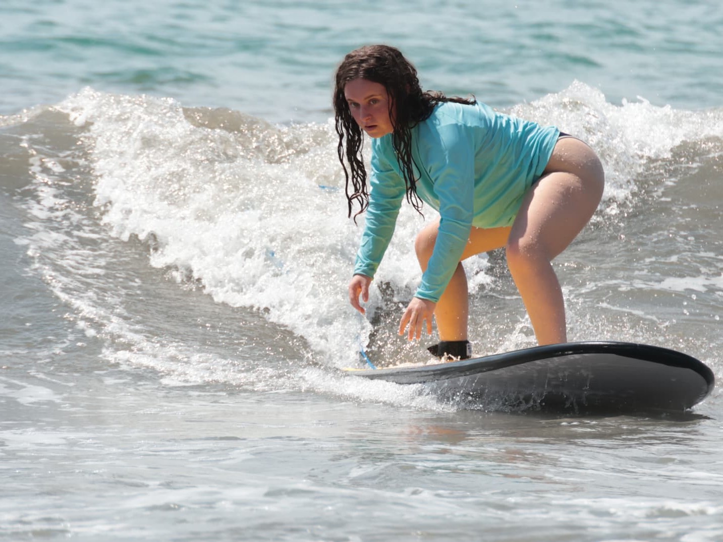 Surfer in a blue Dante's rash guard and yellow shorts balancing on a soft-top at Playa Espadilla